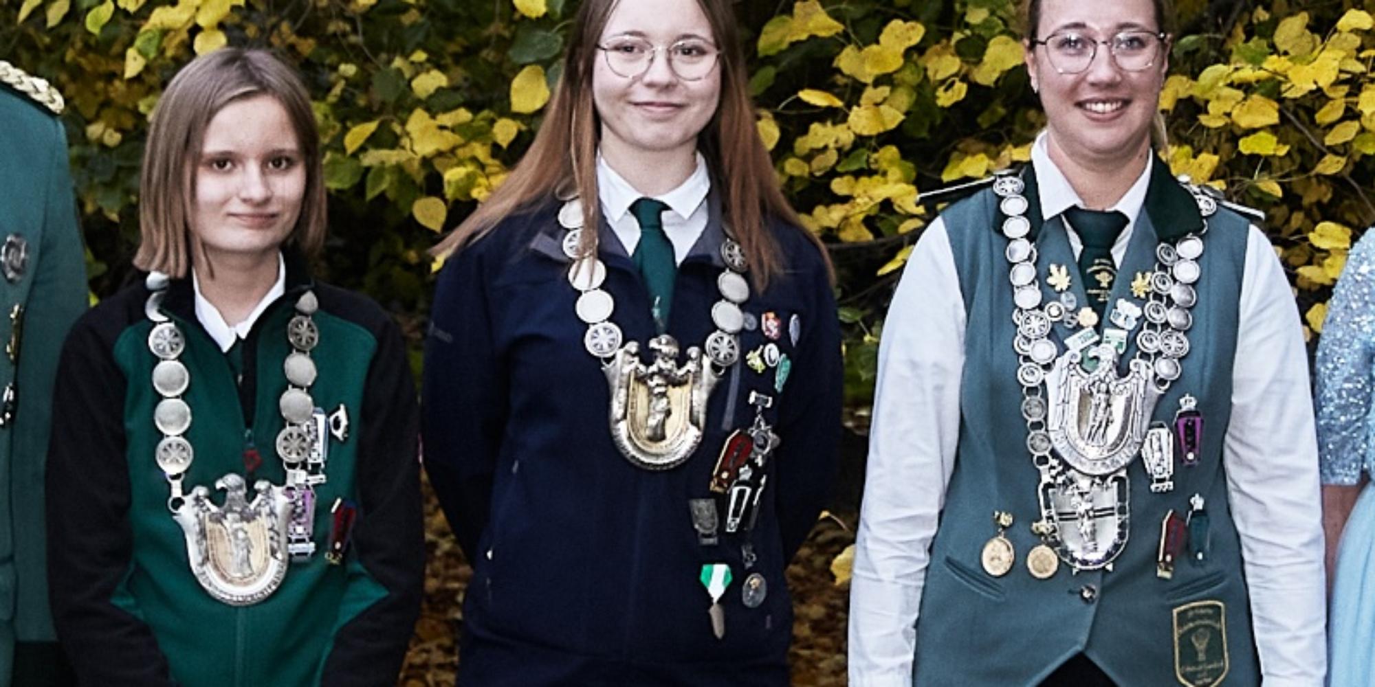 Zu sehen sind die drei neuen Bundesprinzessinen mit ihren Ketten, fotografiert vor einem Gebüsch